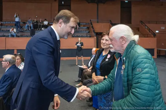 Uroczystość wręczenia odznaczeń, mężczyzna w garniturze podaje rękę starszemu mężczyźnie.