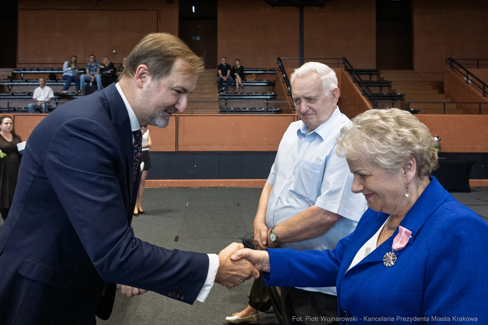 Spotkanie z uściskiem dłoni, dwie osoby w tle obserwują.  Autor: Piotr Wojnarowski