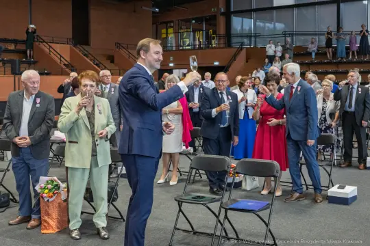 Uroczystość wręczenia odznaczeń, goście w eleganckich strojach wznoszą kieliszki.