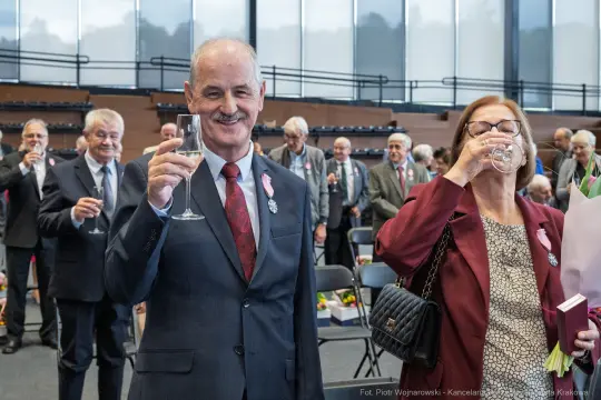 Uczestnicy uroczystości wznoszą toast, w tle widoczni goście.