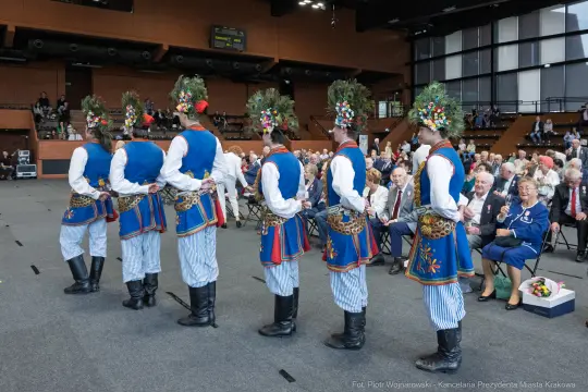 Grupa tancerzy w tradycyjnych strojach ludowych z kwiatowymi wiankami na głowach.