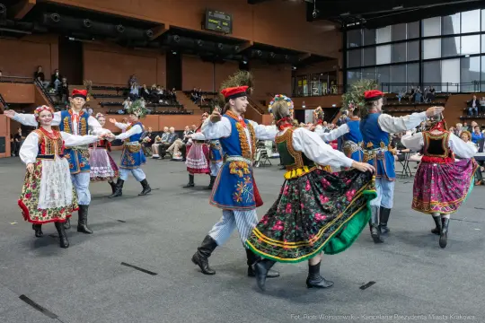 Tancerze w tradycyjnych strojach ludowych tańczą w sali.