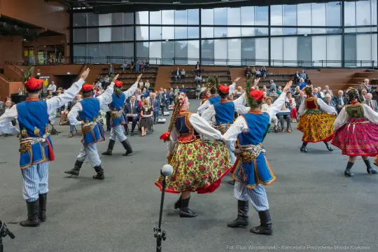 Tancerze w tradycyjnych strojach ludowych tańczą na scenie podczas występu.
