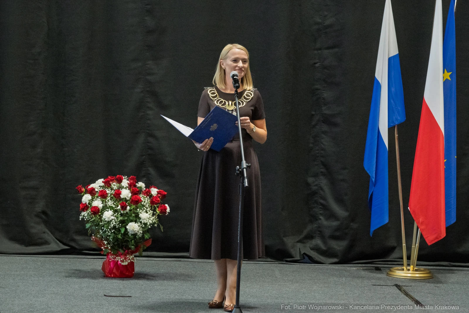 Kobieta w czarnej sukience przemawia do publiczności, obok flagi i bukietu kwiatów.  Autor: Piotr Wojnarowski