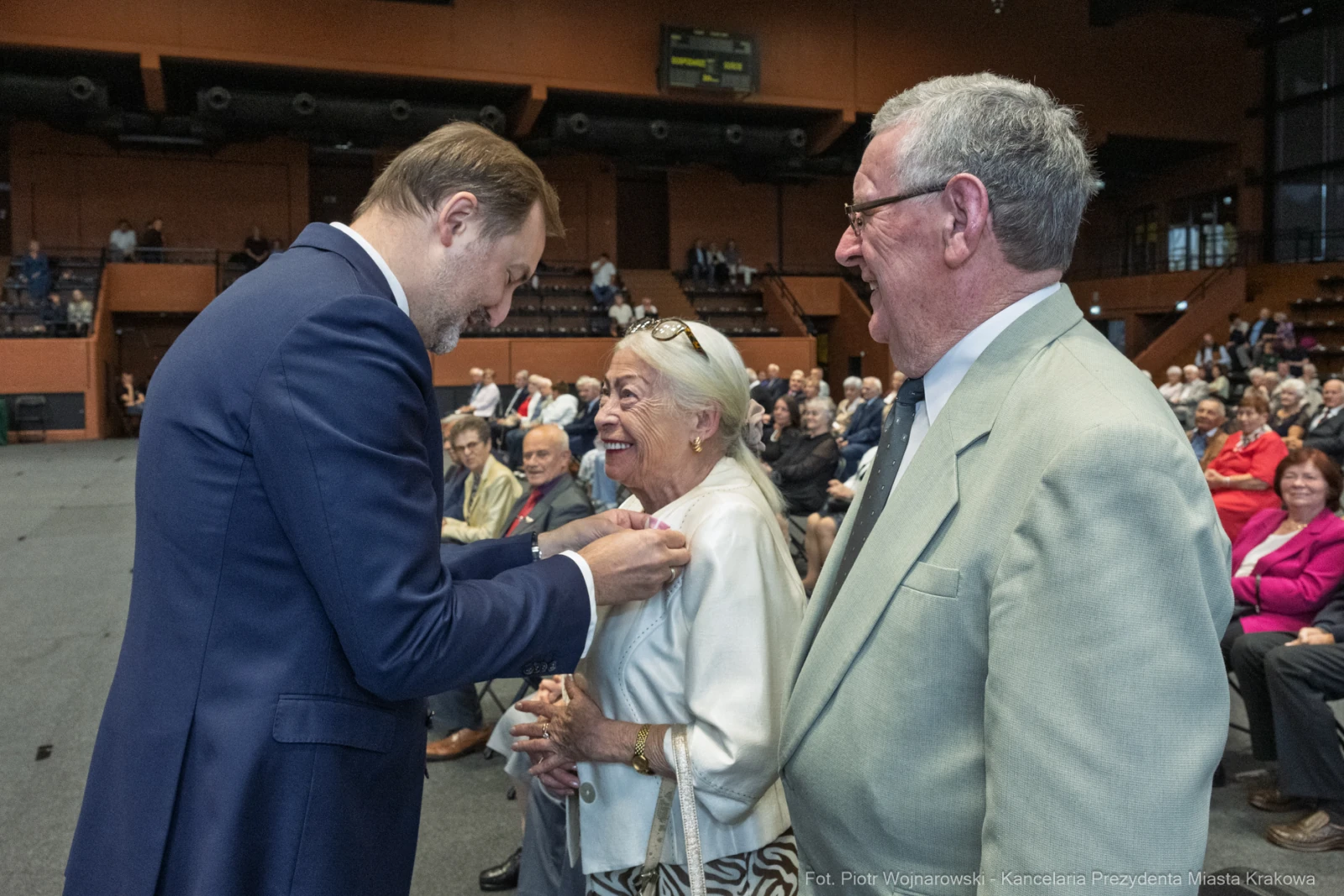 Uśmiechnięci ludzie podczas wręczenia odznaczeń w sali pełnej widzów.  Autor: Piotr Wojnarowski