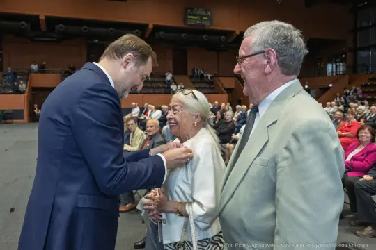 Uśmiechnięci ludzie podczas wręczenia odznaczeń w sali pełnej widzów.