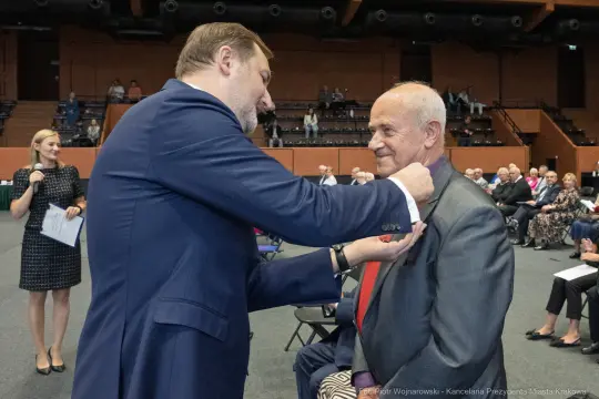 Wręczenie odznaczenia mężczyźnie w garniturze podczas uroczystości.