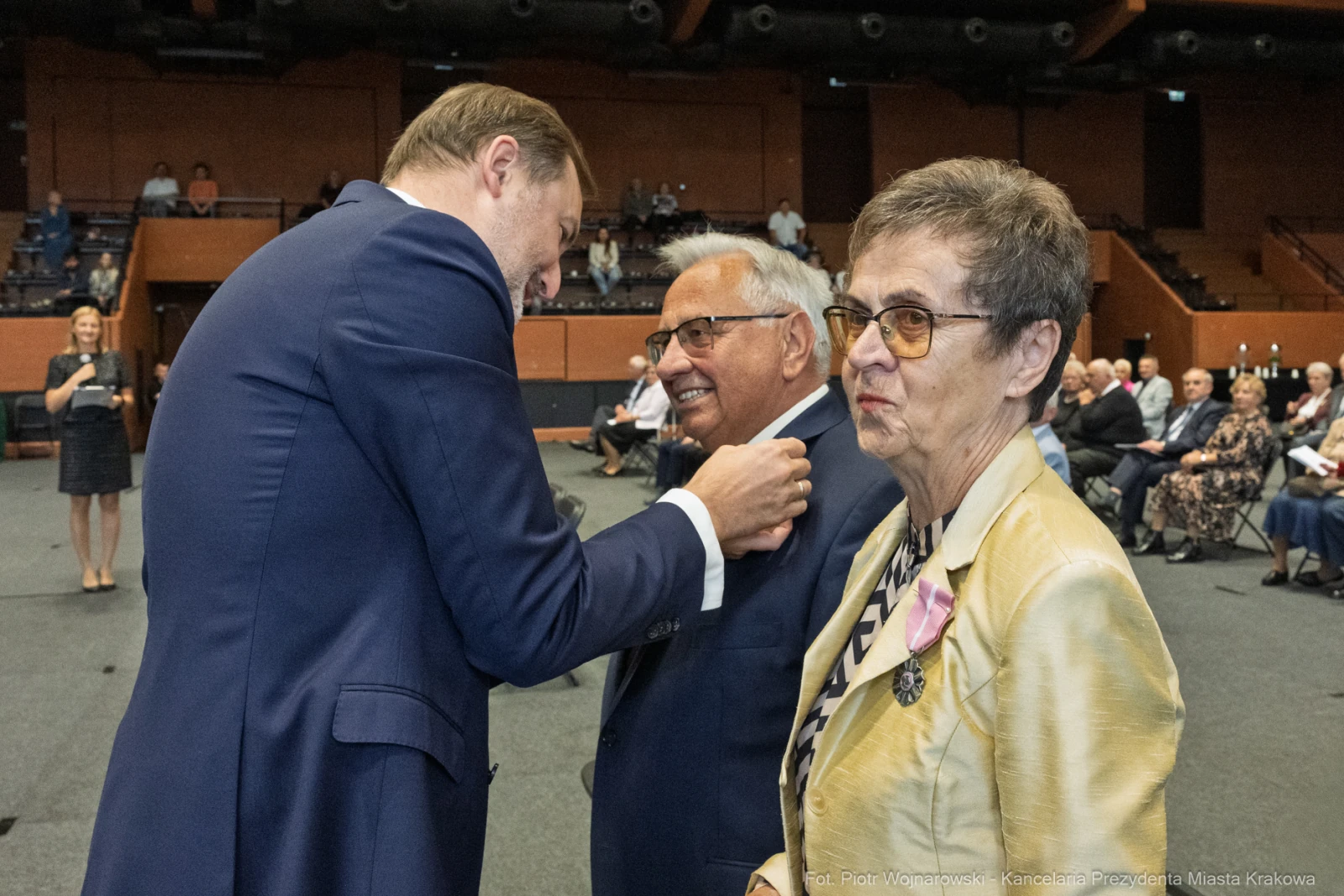 Wręczenie odznaczenia mężczyźnie w garniturze, obok kobieta w okularach i mężczyzna w koszuli.  Autor: Piotr Wojnarowski
