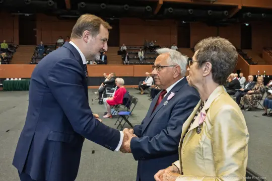 Uroczystość wręczenia odznaczeń, mężczyzna w garniturze wita odznaczonych.
