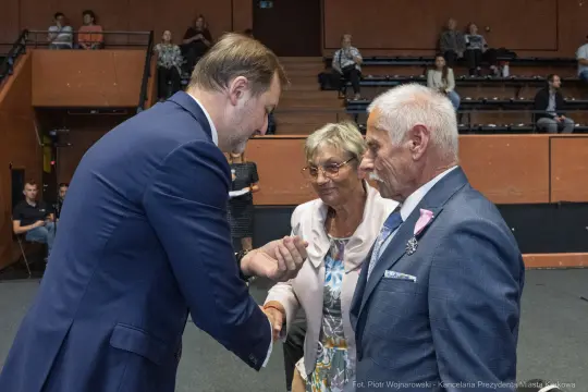 Uścisk dłoni między mężczyzną a parą starszych osób w sali.