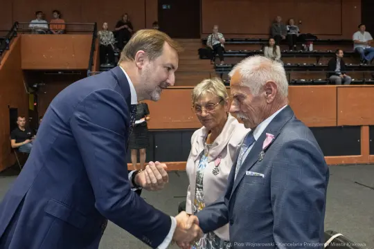 Wręczenie odznaczeń przez mężczyznę w garniturze dwóm starszym osobom.