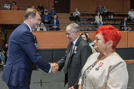 Wręczenie odznaczeń, uściski dłoni, osoby w formalnych strojach.