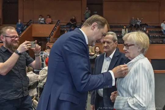 Mężczyzna przypina odznaczenie do ubrania kobiety w towarzystwie innych osób.