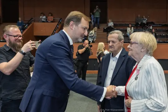Spotkanie mężczyzny w garniturze z dwiema starszymi osobami, uściski dłoni i rozmowy.