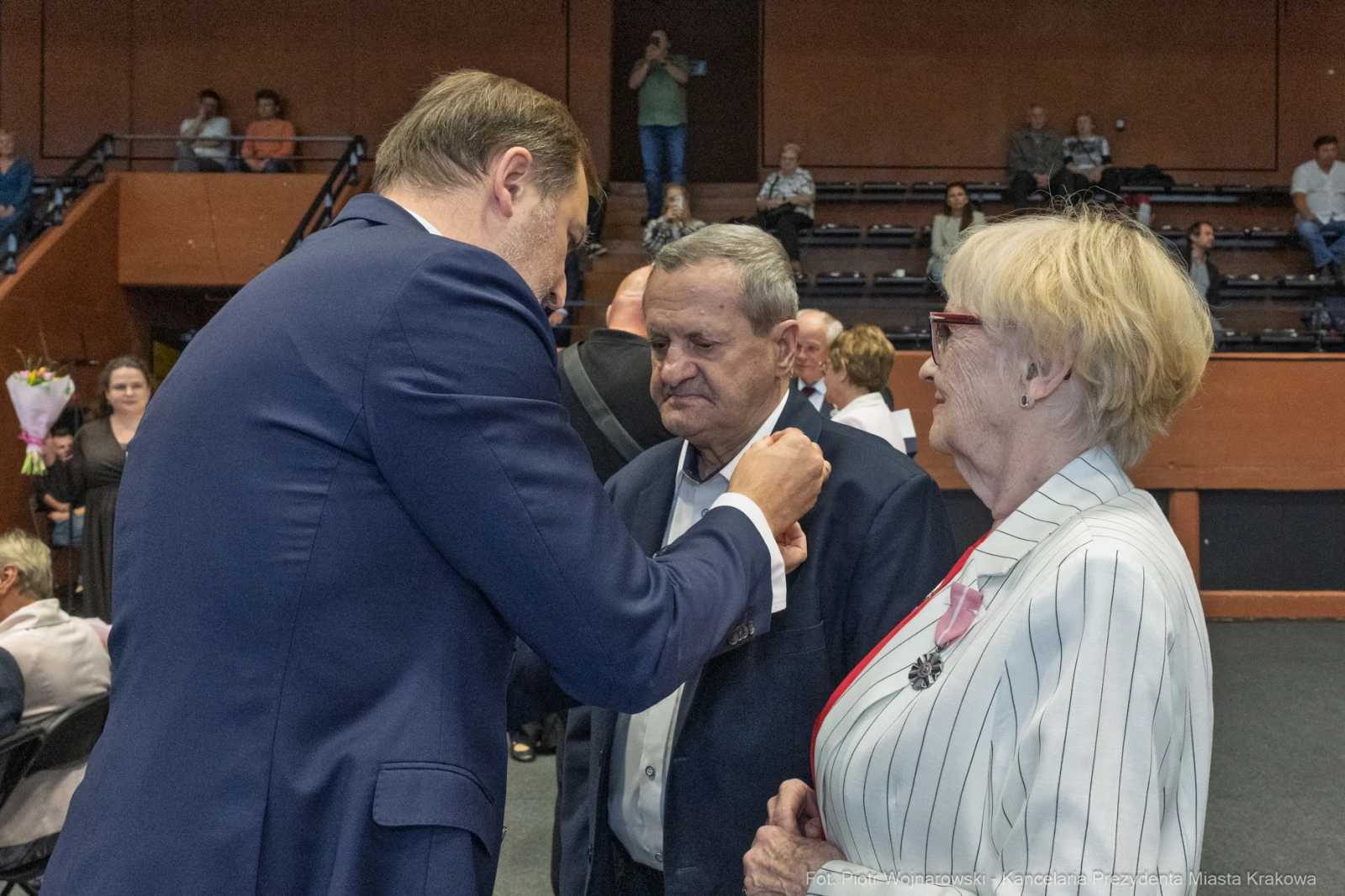 Wręczenie odznaczenia mężczyźnie przez mężczyznę w garniturze, obok kobieta w okularach.  Autor: Piotr Wojnarowski