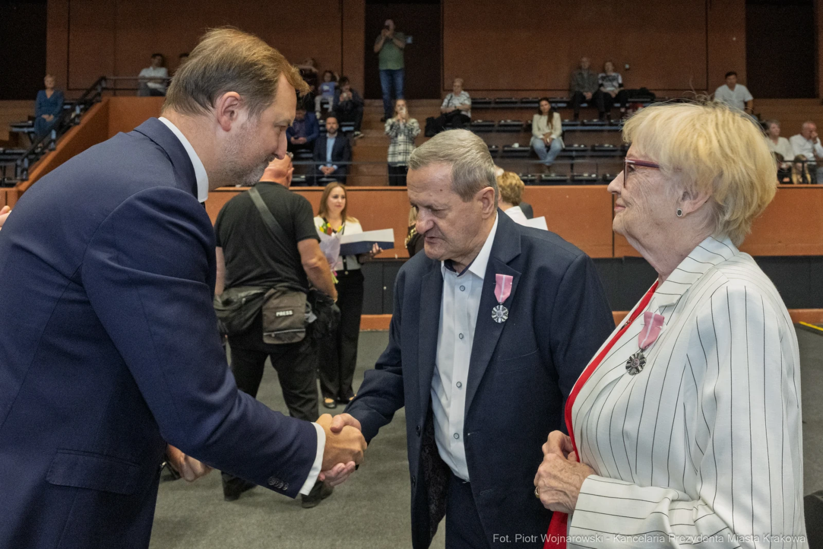Uścisk dłoni między mężczyzną a starszymi osobami, w tle widownia.  Autor: Piotr Wojnarowski