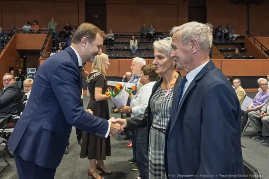 Uroczystość wręczenia nagród, uściski dłoni i kwiaty w rękach uczestników.