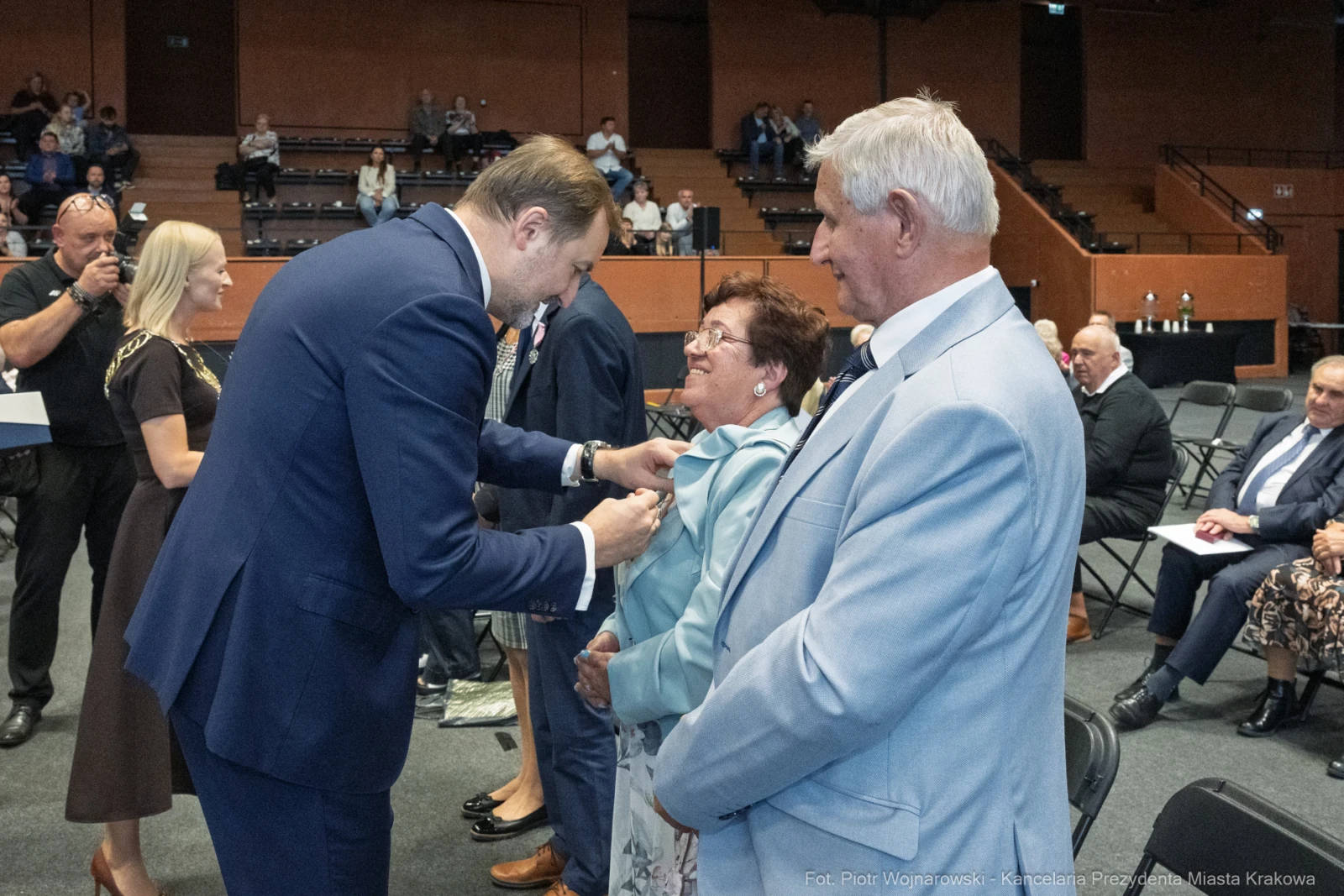 Wręczenie odznaczenia przez mężczyznę starszej kobiecie w towarzystwie mężczyzny w jasnym garniturze.  Autor: Piotr Wojnarowski