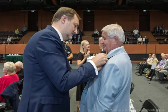 Ceremonia wręczenia odznaczeń, mężczyzna przypina medal innemu mężczyźnie.