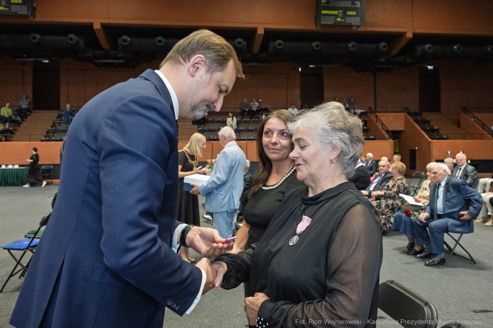 Wręczenie odznaczenia przez mężczyznę starszej kobiecie w obecności innych gości.  Autor: Piotr Wojnarowski