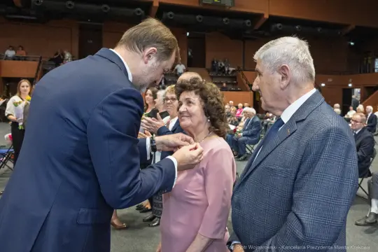 Uroczystość wręczenia odznaczeń, osoby w eleganckich strojach, emocjonalne chwile.