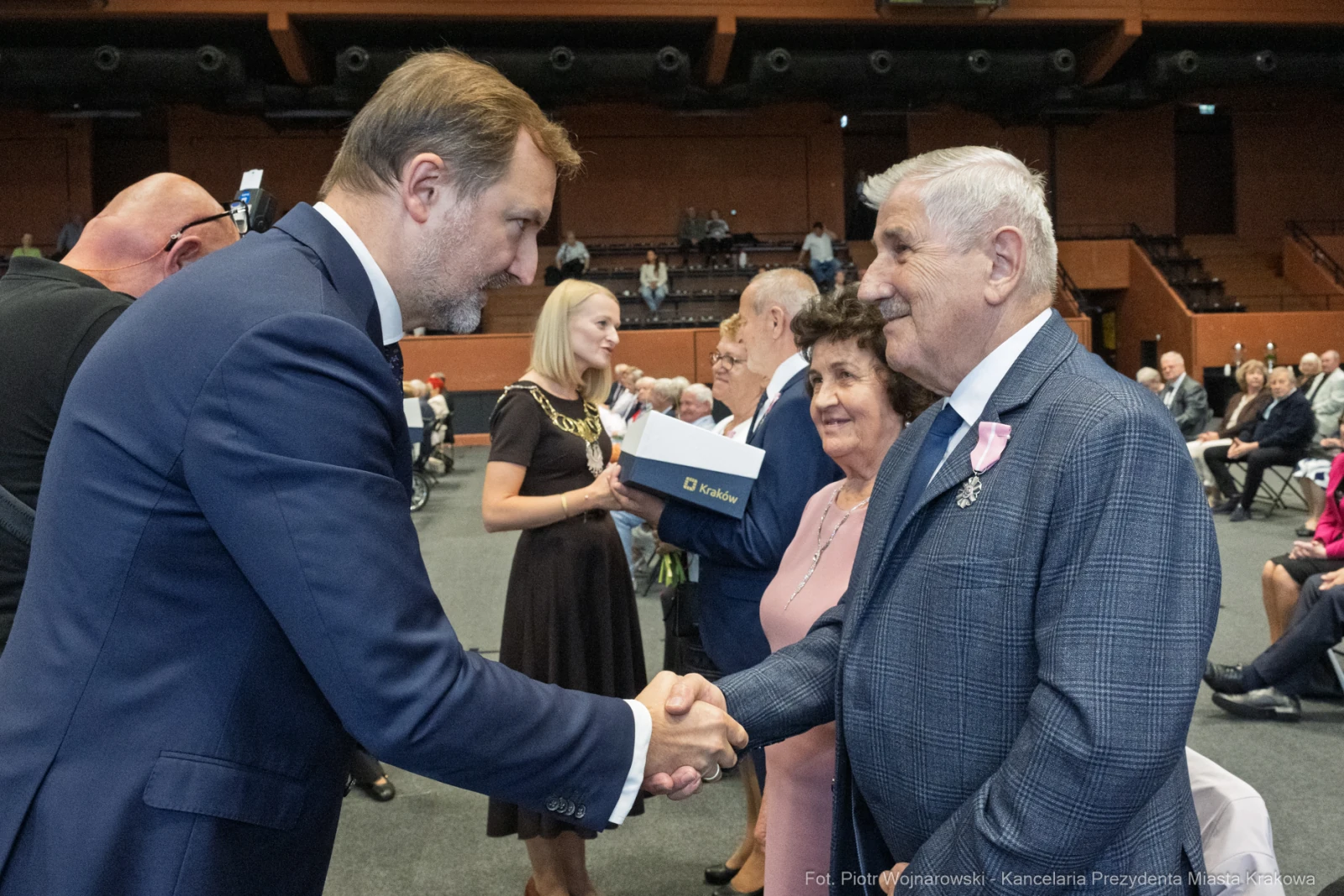 Mężczyzna w garniturze podaje rękę starszemu mężczyźnie z wąsami, w tle inni uczestnicy wydarzenia.  Autor: Piotr Wojnarowski