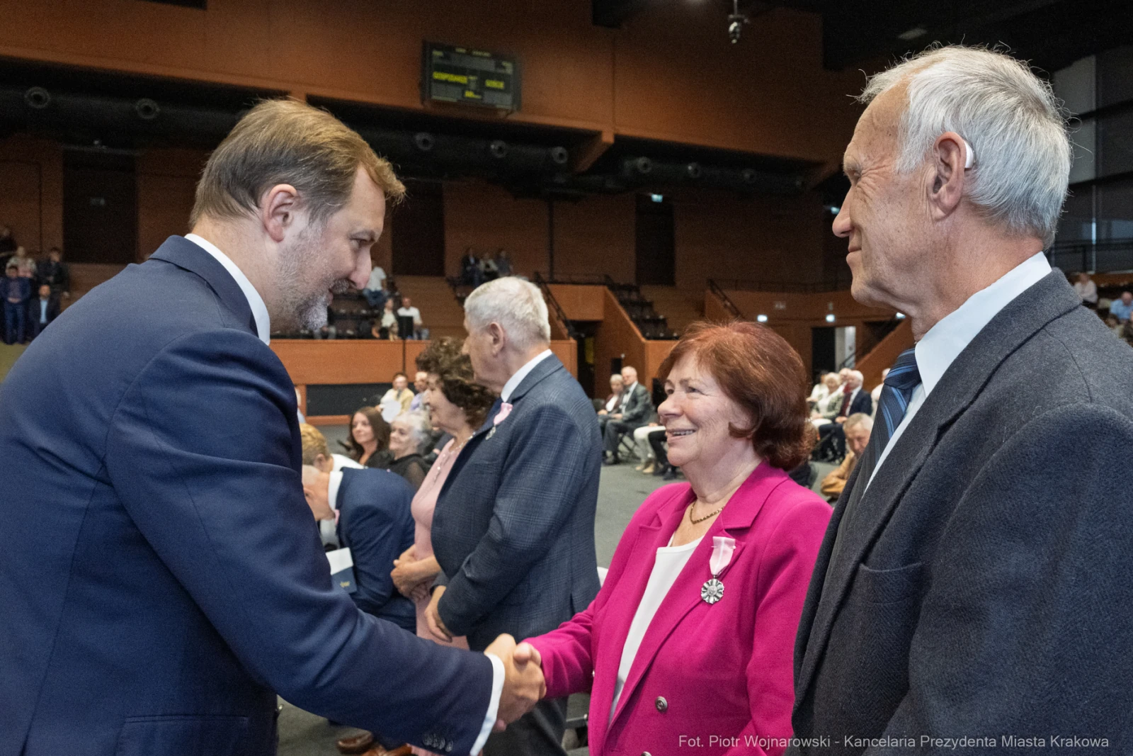 Uścisk dłoni między mężczyzną a kobietą w sali konferencyjnej, w tle zgromadzeni goście.  Autor: Piotr Wojnarowski