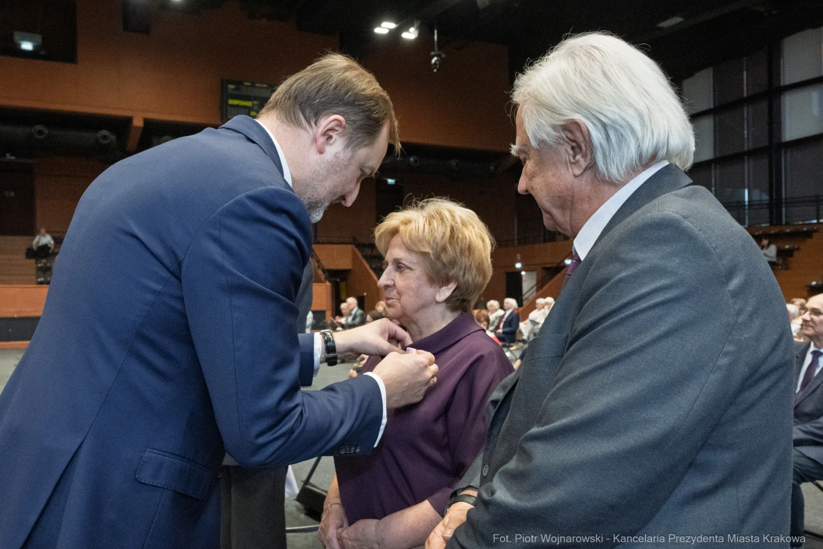 Wręczenie odznaczenia przez mężczyznę starszej kobiecie w obecności drugiego mężczyzny.  Autor: Piotr Wojnarowski