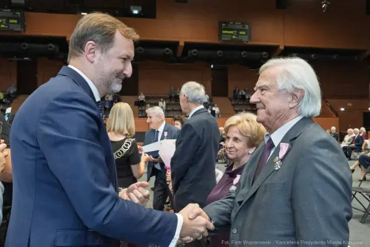 Uroczystość wręczenia odznaczeń, uściski dłoni i uśmiechy uczestników.
