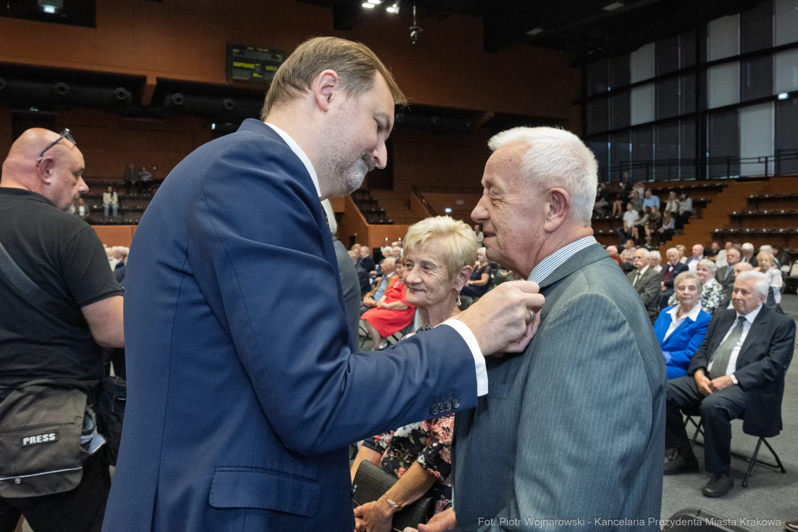 Mężczyzna przypina odznaczenie starszemu mężczyźnie w towarzystwie innych osób.  Autor: Piotr Wojnarowski
