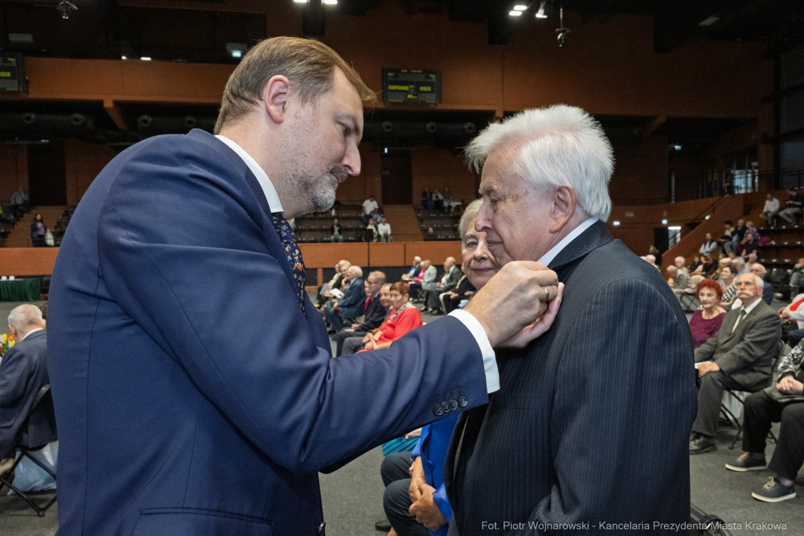 Mężczyzna przypina odznaczenie innemu mężczyźnie podczas uroczystości.  Autor: Piotr Wojnarowski