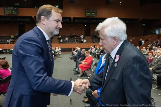 Uścisk dłoni dwóch mężczyzn podczas wydarzenia w sali konferencyjnej.