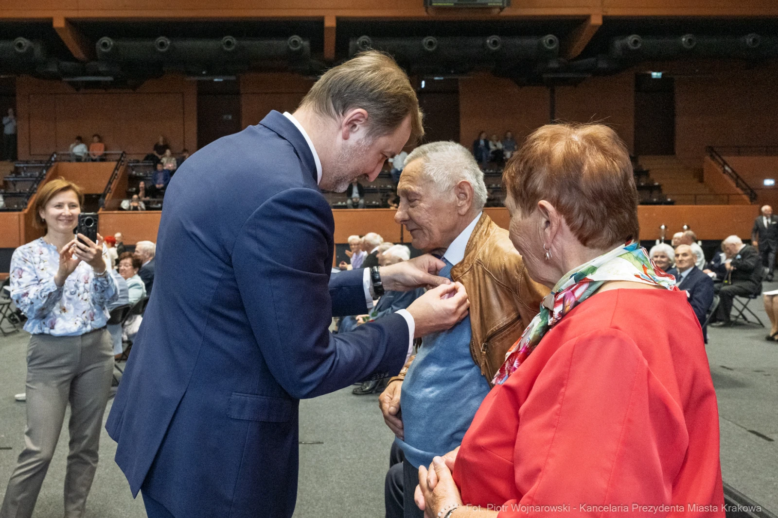 Wręczenie odznaczenia starszemu mężczyźnie podczas uroczystości w sali. Obecni goście w tle.  Autor: Piotr Wojnarowski