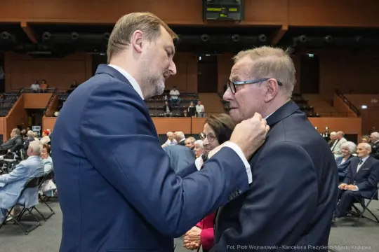 Dwaj mężczyźni rozmawiają w sali wypełnionej innymi uczestnikami wydarzenia.