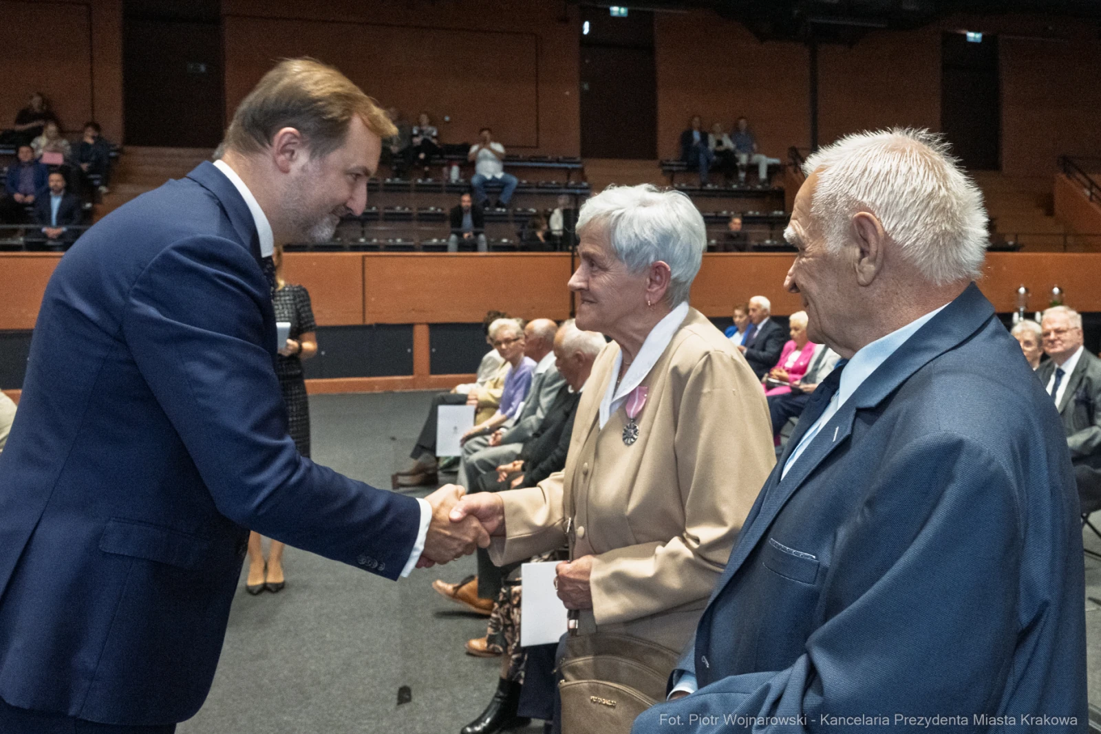 Uroczystość wręczenia odznaczeń, uściski dłoni, starsze osoby w sali.  Autor: Piotr Wojnarowski