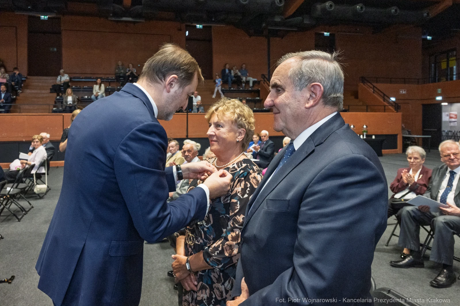 Wręczenie odznaczenia przez mężczyznę kobiecie w towarzystwie drugiego mężczyzny na uroczystości.  Autor: Piotr Wojnarowski