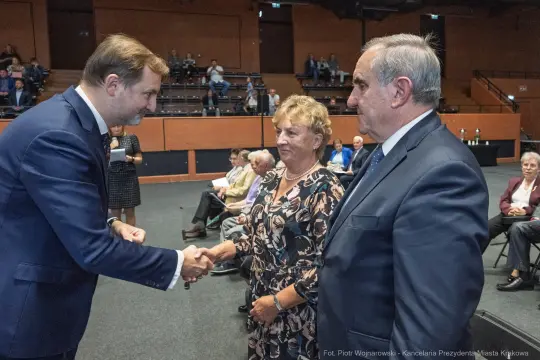 Spotkanie trzech osób, w tym mężczyzny w garniturze, podczas uroczystości.