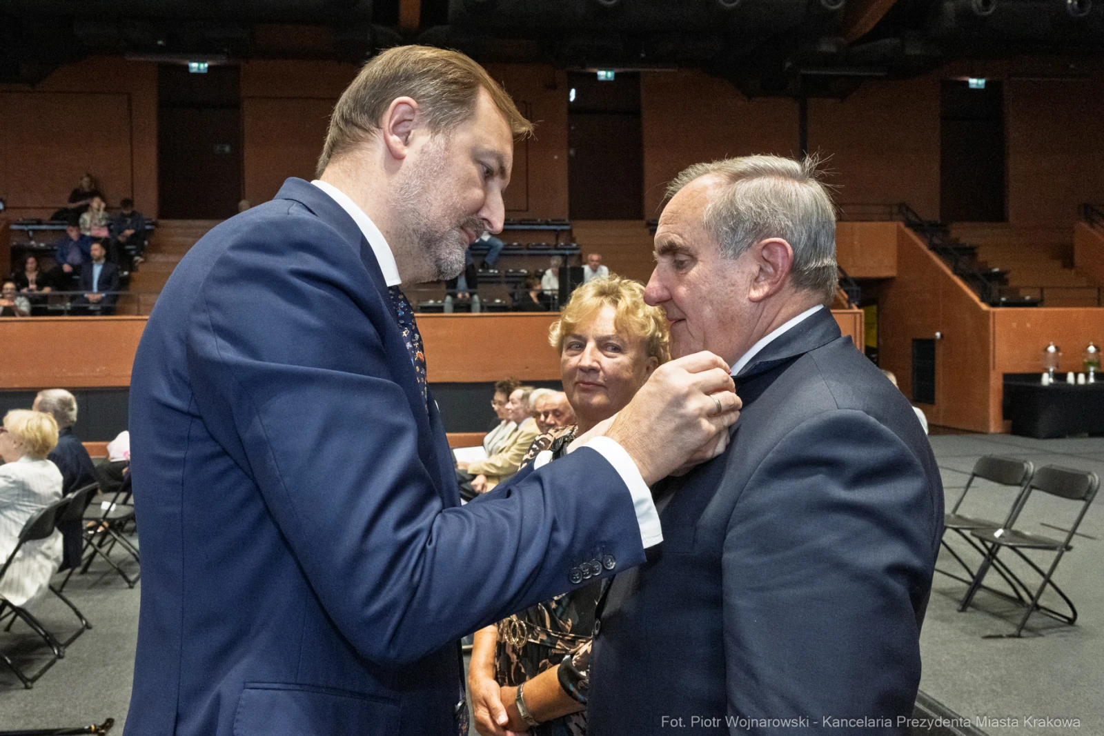Wręczenie odznaczenia mężczyźnie przez innego mężczyznę, w tle kobieta i publiczność.  Autor: Piotr Wojnarowski