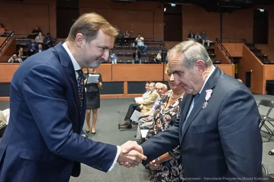 Mężczyźni uściskiem dłoni wymieniają się gratulacjami w formalnej atmosferze.