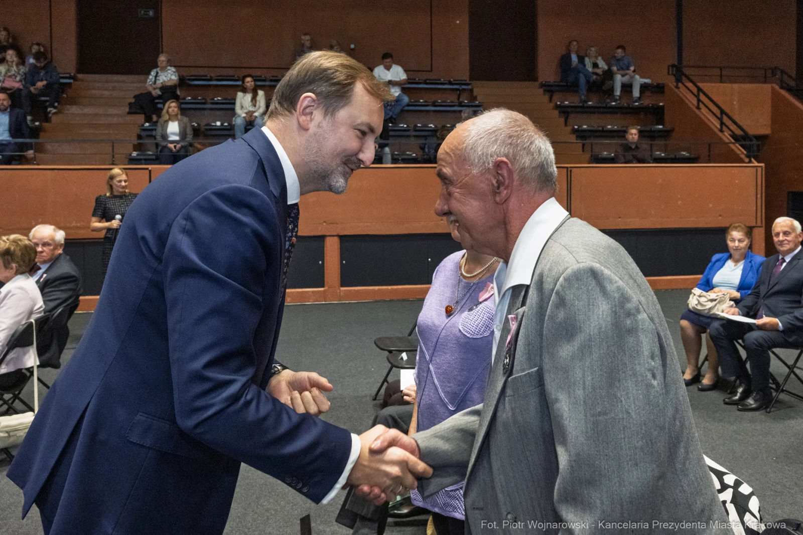 Uścisk dłoni dwóch mężczyzn podczas wydarzenia w sali. W tle widoczni uczestnicy.  Autor: Piotr Wojnarowski