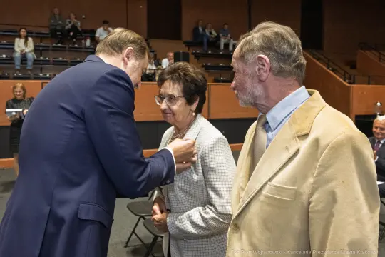 Wręczenie odznaczenia kobiecie przez mężczyznę w formalnym otoczeniu.
