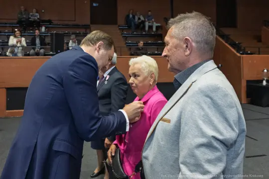 Wręczenie odznaczeń w sali obrad, uczestnicy w formalnych strojach.