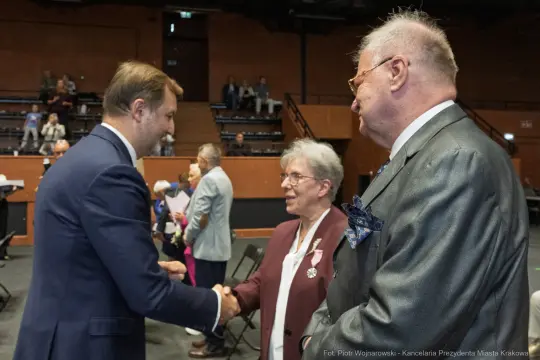 Spotkanie trzech osób, jedna z nich w garniturze, uściski dłoni i rozmowy.