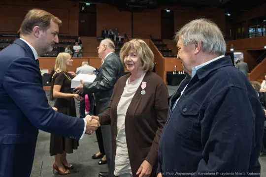Uroczystość wręczenia odznaczeń, uściski dłoni i uśmiechy uczestników.