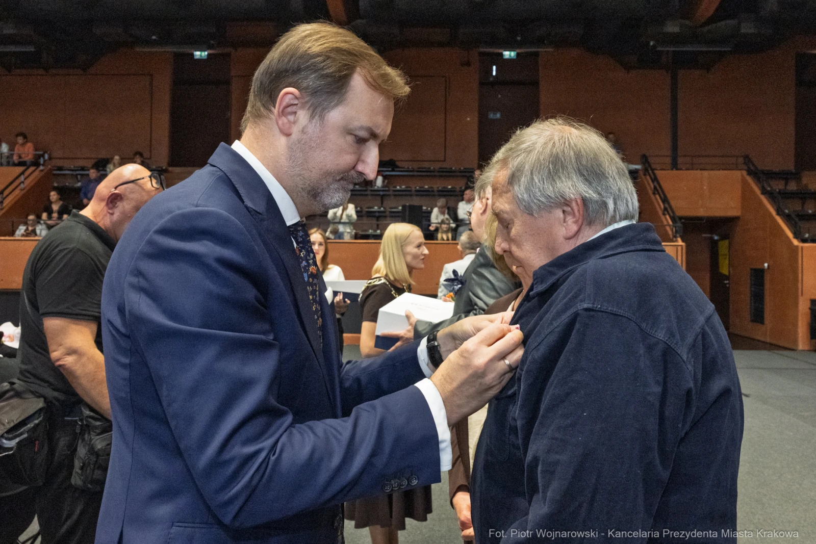 Wręczenie odznaczenia przez mężczyznę w garniturze drugiemu mężczyźnie w ciemnej odzieży.  Autor: Piotr Wojnarowski
