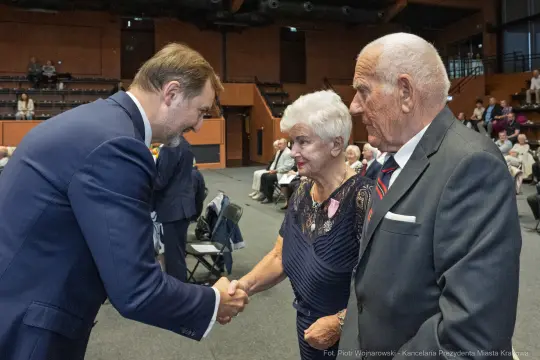 Uścisk dłoni między mężczyzną a starszą parą w sali pełnej ludzi.