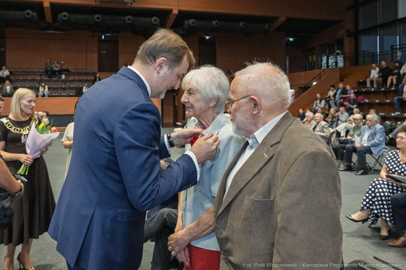 Uroczystość wręczenia odznaczeń, starsza para w rozmowie z mężczyzną w garniturze.  Autor: Piotr Wojnarowski