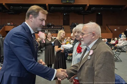 Uroczystość wręczenia odznaczeń, uściski dłoni i obecność gości w sali.