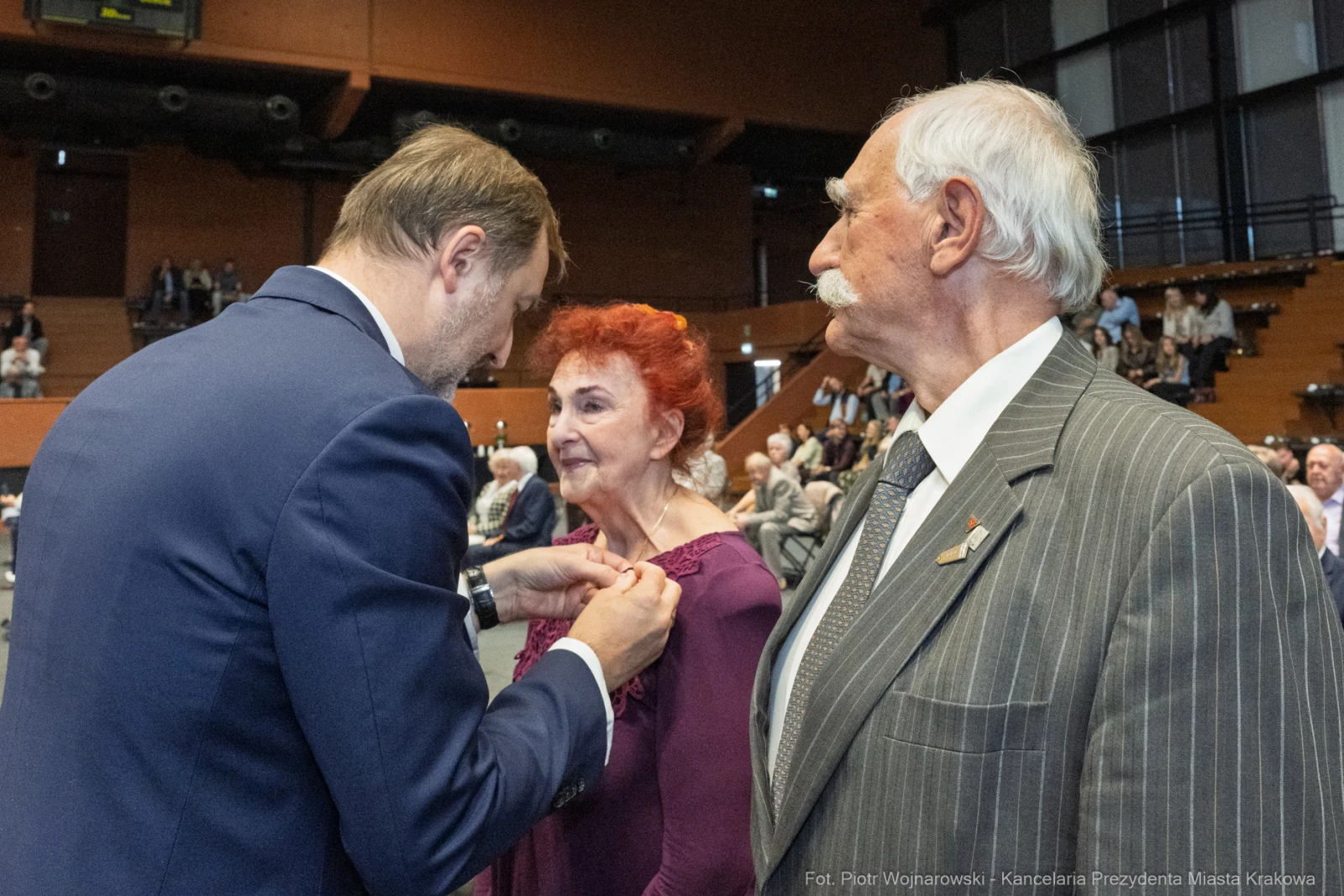 Wręczenie odznaczenia kobiecie przez mężczyznę w towarzystwie starszego mężczyzny.  Autor: Piotr Wojnarowski