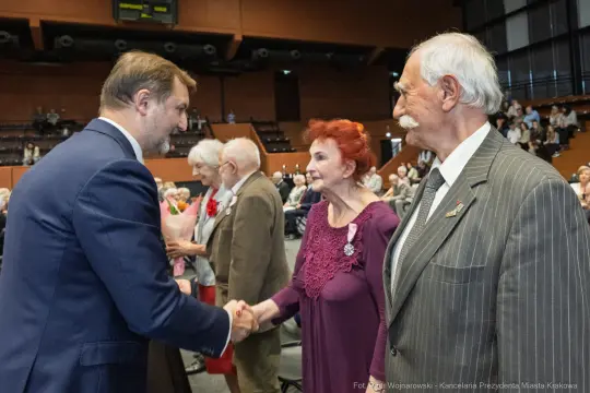 Uroczystość wręczenia odznaczeń, uściski dłoni i wzruszone twarze uczestników.